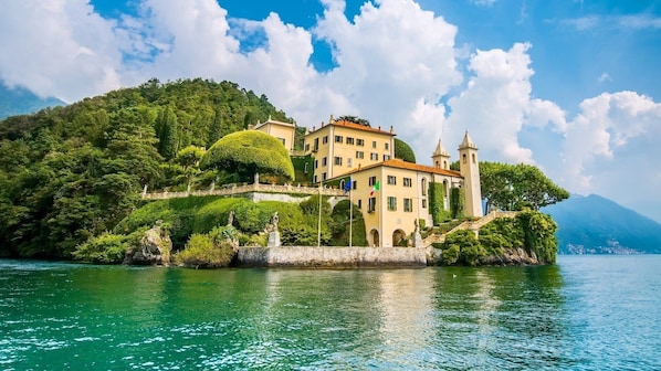 A historic building with a tower, situated on a lush green hillside by a clear blue lake.