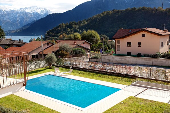 Une piscine dotée d’une terrasse en bois, entourée d’une clôture en métal, avec en toile de fond des montagnes et un lac.