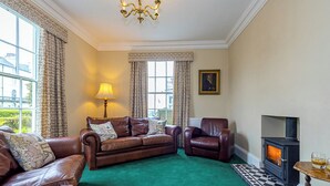 A living room with a green carpet, leather sofas, a fireplace, and a chandelier. - 3 bedroom accommodation in Filey (Filey)