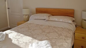 Uma cama bem arrumada com colcha estampada, duas luminárias de cabeceira e uma cabeceira de madeira.
