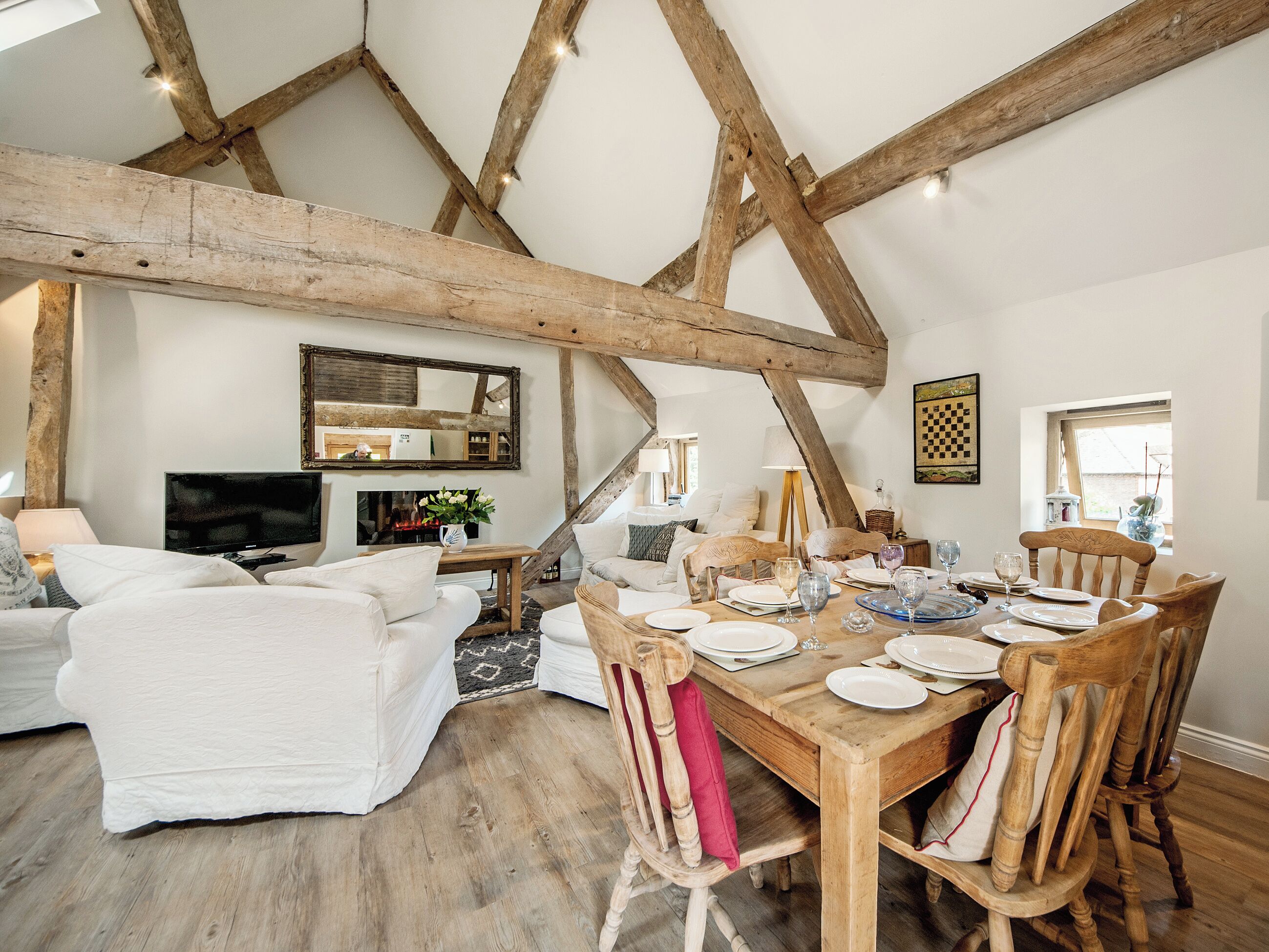 Een eetruimte met een houten tafel voor vier personen, omringd door houten stoelen. Een televisie is aan de muur boven de zithoek bevestigd.