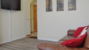 Una sala de estar con un sofá de cuero marrón, un cojín rojo y tres cuadros en la pared.
