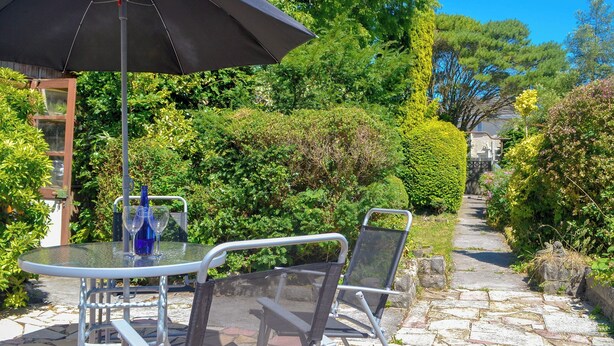 Un patio con una mesa, sillas, un paraguas negro y un sendero de piedra.
