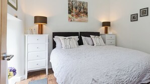 Une chambre avec un grand lit, deux tables de chevet, une commode, un tableau au mur et une porte avec une petite pancarte.