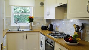Una cocina con lavadora, estufa, pileta y ventana con vista a árboles.