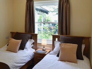 Ein Doppelzimmer mit zwei Betten, einem Nachttisch mit Lampe und einem Fenster mit Vorhängen.