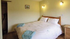 A bedroom with a wooden bed, two bedside lamps, a small bedside table, and a picture on the wall. - Quaint, cosy and comfortable… The Brewhouse is just that. (Foxham)