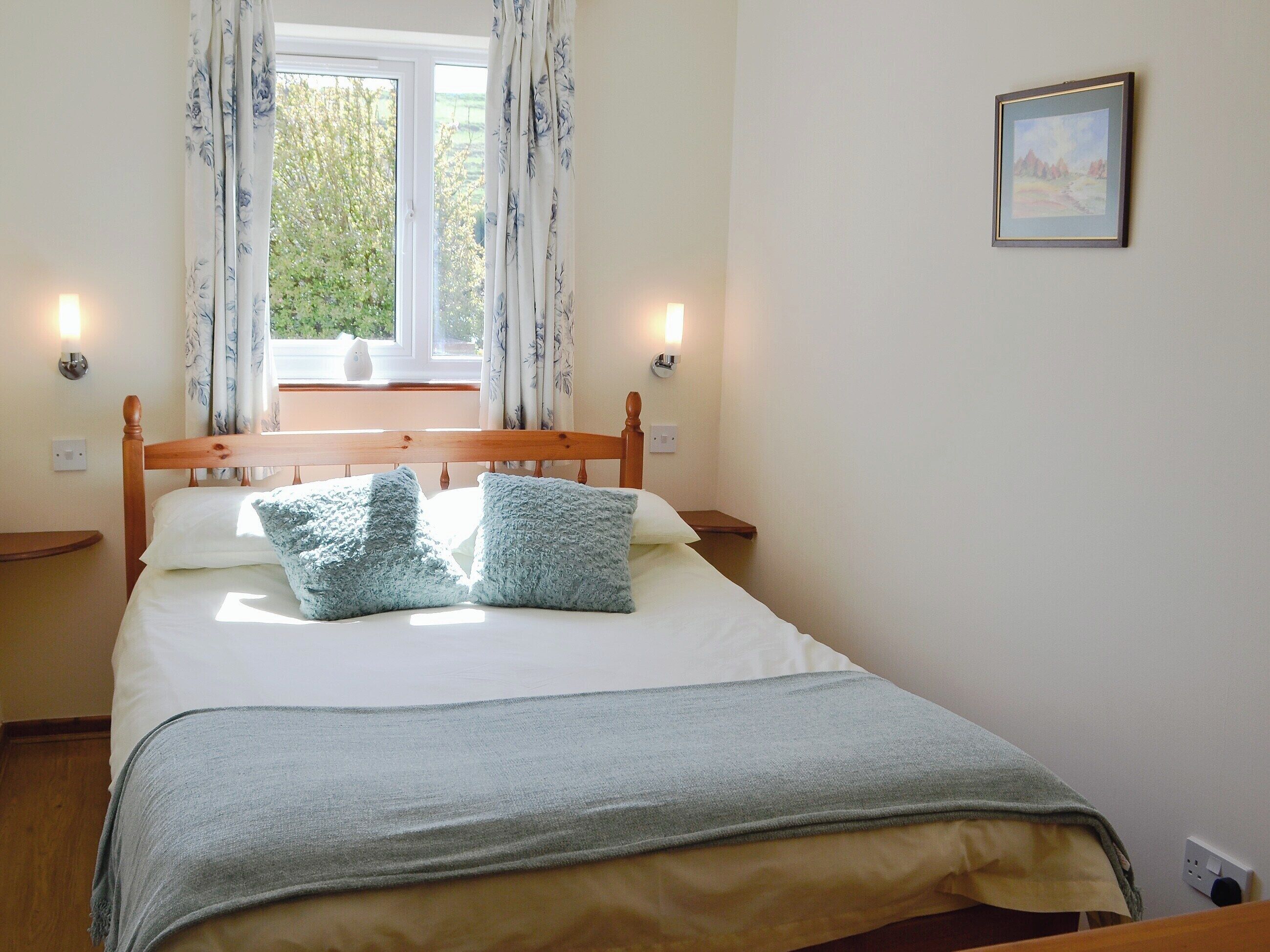 A neatly made bed with a wooden headboard, two bedside tables, and a window with curtains.