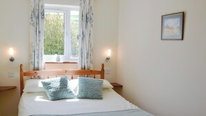Een net opgemaakt bed met een houten hoofdbord, twee nachtkastjes en een raam met gordijnen.