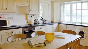 Een keuken met witte kastjes, een magnetron, een spoelbak en een tafel met stoelen.
