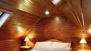 Een kamer met houten lambrisering en een schuine kap, een bed met bloemenprint beddengoed, twee nachtkastjes met lampen, en een raam.