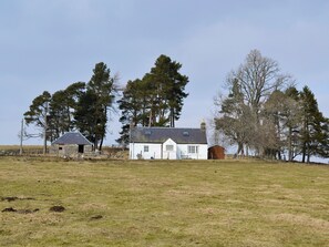 A white house with a grey roof, surrounded by a grassy field and trees.