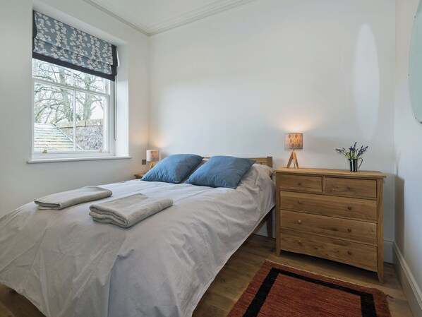 Una camera da letto con un letto, comodini, abat-jour e una finestra vista alberi.