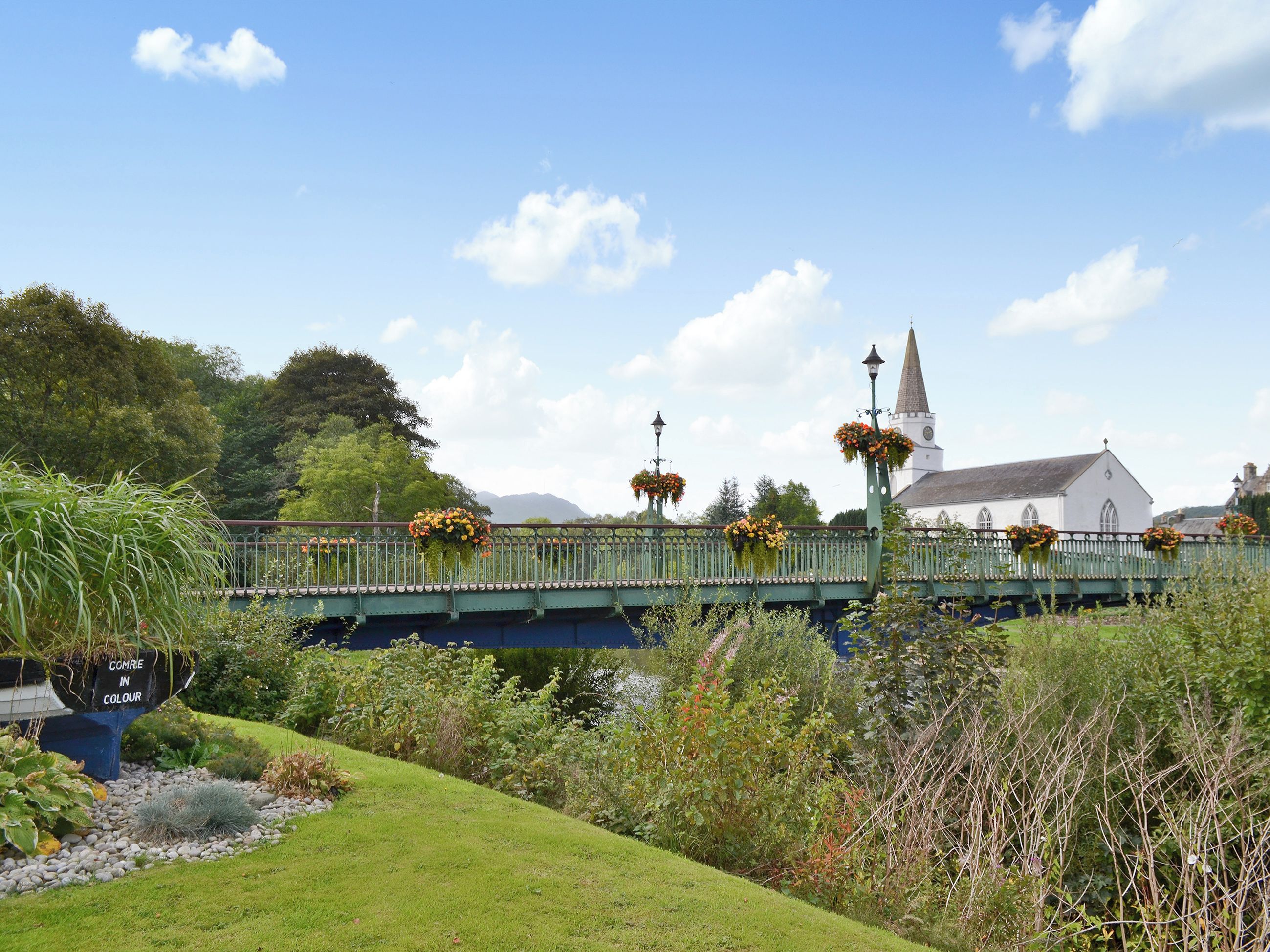 Un pont verdoyant orné de jardinières fleuries, une église et une végétation luxuriante.