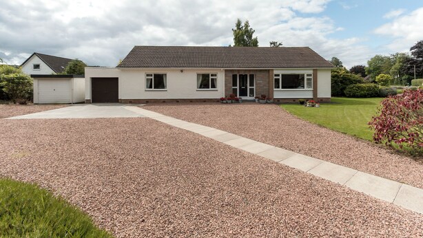A single-story house with a gravel driveway, a garage, and a lawn.
