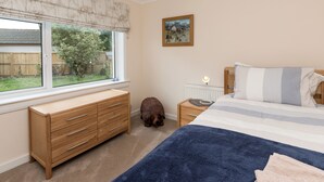 A bedroom with a large window, a wooden dresser, a dog, a bedside table with a lamp, and a bed with striped bedding.