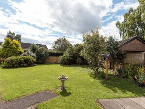 A backyard with a wooden fence, a bird bath, and various shrubs and trees. - 2 bedroom accommodation in Comrie, near Crieff (Comrie, near Crieff)