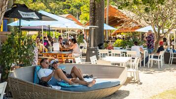 Un salon de plage avec des fauteuils et des tables en osier, des parasols et une vue sur l’océan.