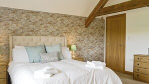 A bedroom with a stone wall, a wooden ceiling, a bed with white bedding, a bedside table with a lamp, and a wooden wardrobe.
