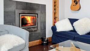A living room with a fireplace, a guitar, a sofa, and a glass coffee table. - 2 bedroom accommodation in Buckie, near Cullen (Buckie, near Cullen)