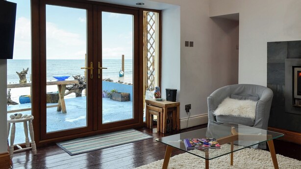 A living room with a glass coffee table, a grey armchair, and a fireplace. - 2 bedroom accommodation in Buckie, near Cullen (Buckie, near Cullen)