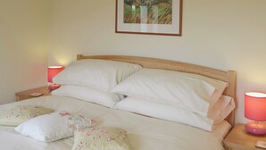 A neatly made bed with white linens and floral pillows, two bedside lamps, and a framed landscape painting on the wall. - 2 bedroom accommodation in Pendeen (Pendeen)