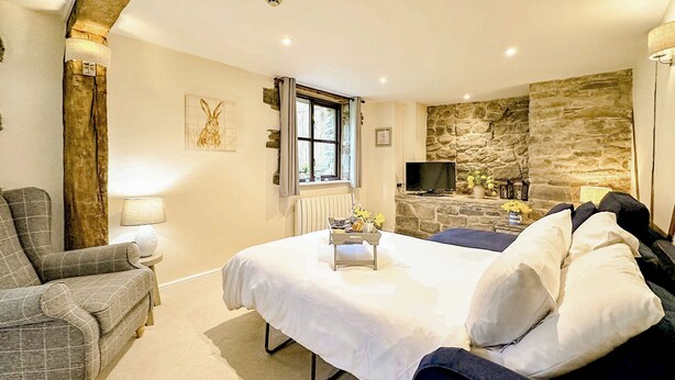 Een slaapkamer met een bed, een stoel, een televisie en een stenen muur.