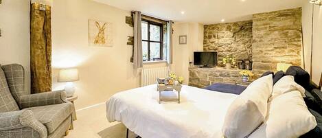 A bedroom with a bed, a chair, a television, and a stone wall.