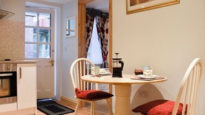 Een eetgedeelte met een houten tafel en stoelen, een koffiezetapparaat, en een ingelijst schilderij aan de muur.