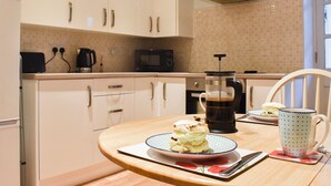 Een keuken met witte kasten, een magnetron, een koffiezetapparaat en een tafel met een bord scones en een mok.