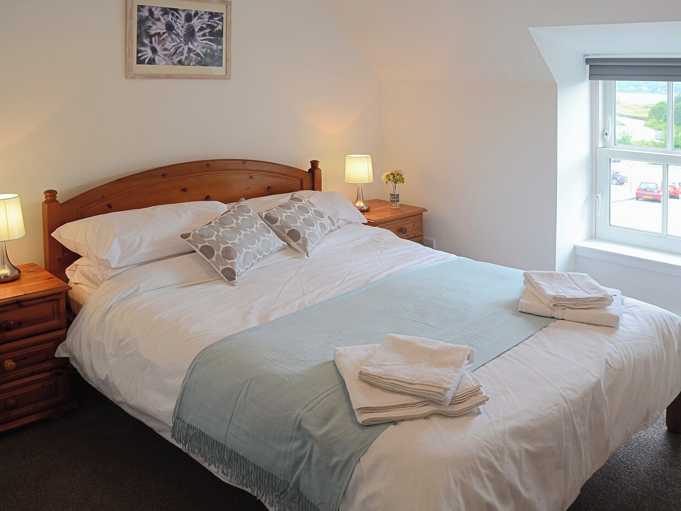 A neatly made bed with pillows, a bedside lamp, a nightstand, and a window with a view of a river.