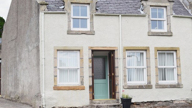 A two-story house with a stone facade, a green door, and multiple windows with white frames. - 2 bedroom accommodation in Bonar Bridge (Bonar Bridge)