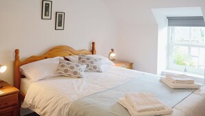 A neatly made bed with pillows, a bedside lamp, and a window with a view of greenery. - 2 bedroom accommodation in Bonar Bridge (Bonar Bridge)