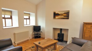 A living room with a sofa, a coffee table, a fireplace, a television, and a radiator.