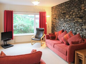A living room with a stone wall, a red sofa, a leather chair, and a television on a stand.