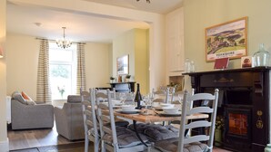 A dining area with a wooden table set for four, surrounded by white chairs with cushioned seats. A fireplace with a black mantel is visible in the background. - 3 bedroom accommodation in Horton in Ribblesdale, near Settle (Horton in Ribblesdale, near Settle)