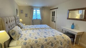 Een slaapkamer met een groot bed, een nachtkastje met lamp, een dressoir, een spiegel en een raam met gordijnen.