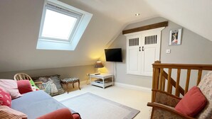 Een knus loft slaapkamer met een schuine plafond, een dakraam, een televisie aan de muur en een houten stoel met kussen.