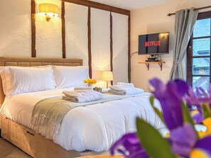 A hotel room with a bed, a television, a lamp, and a window with curtains.