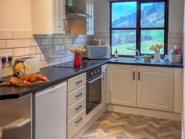A kitchen with white cabinets, a herringbone-patterned floor, a toaster, a microwave, and a window with a view of a green landscape.