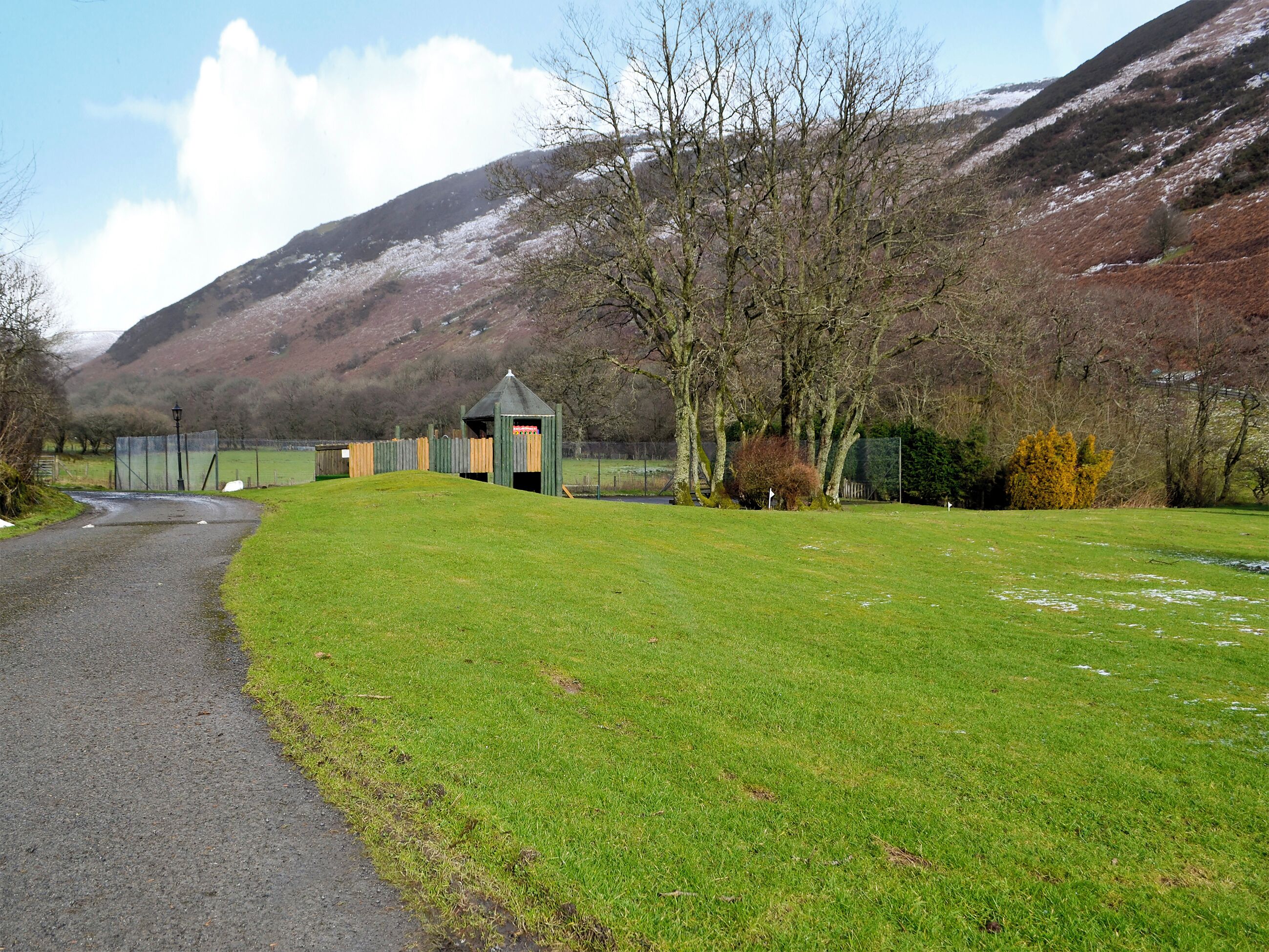 A rural landscape with a gravel path, a small wooden structure, and a grassy field.