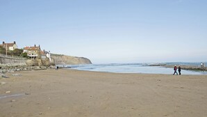 A beach with a stone wall, houses, and a clear sky. - Sharrowhead Cottage - E4044 (Robin Hood&rsquo;s Bay)