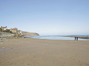 A beach with a stone wall, houses, and a clear sky. - Sharrowhead Cottage - E4044 (Robin Hood’s Bay)