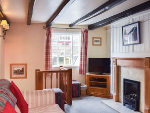 A cozy living room with a fireplace, a television, and a window with curtains. - Sharrowhead Cottage - E4044 (Robin Hood’s Bay)