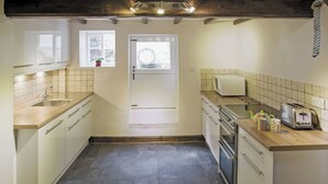 A compact kitchen with a sink, stove, microwave, and toaster. - Sharrowhead Cottage - E4044 (Robin Hood&rsquo;s Bay)