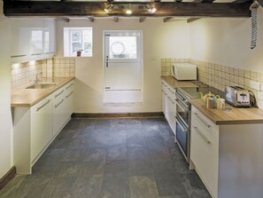 A compact kitchen with a sink, stove, microwave, and toaster. - Sharrowhead Cottage - E4044 (Robin Hood’s Bay)