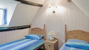A bedroom with two single beds, a nightstand with a lamp, a window with curtains, and wooden paneling on the walls. - Sharrowhead Cottage - E4044 (Robin Hood&rsquo;s Bay)