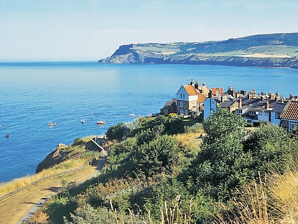 A coastal village with houses along the cliffside, a clear view of the sea, and a pathway leading down to the beach. - Sharrowhead Cottage - E4044 (Robin Hood’s Bay)