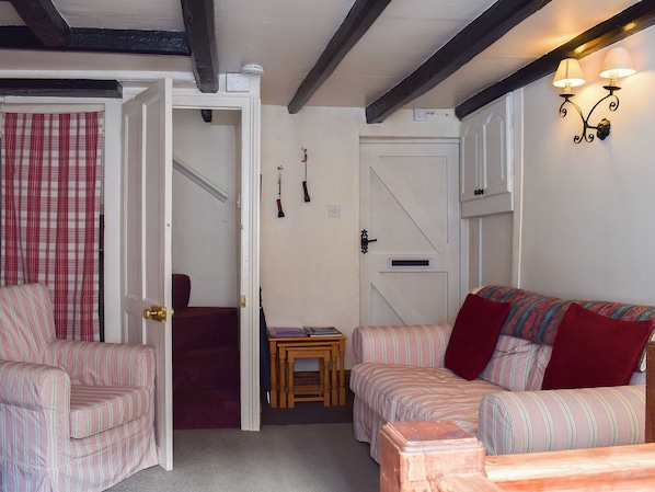 A room with two striped sofas, a small wooden table, a door with a red curtain, and a wall-mounted light fixture. - Sharrowhead Cottage - E4044 (Robin Hood’s Bay)