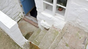 A white building with a blue door and a window with a potted plant. - Sharrowhead Cottage - E4044 (Robin Hood&rsquo;s Bay)